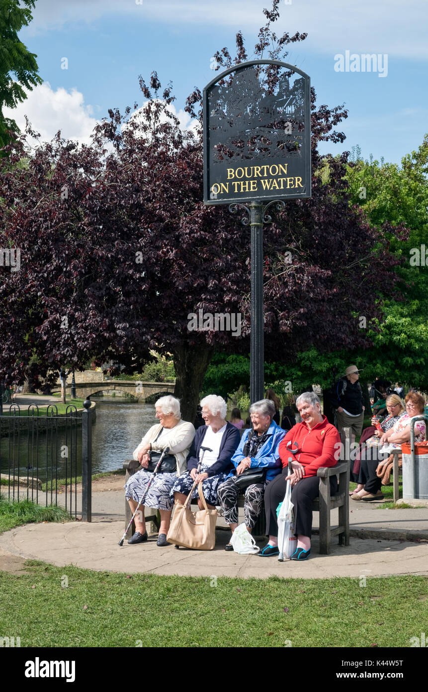 Eine Gruppe von Rentnern genießen sitzen auf einer Bank neben dem Fluss Windrush, unterhalb der bourton auf dem Wasser Zeichen in der Mitte des historischen Dorfes Stockfoto