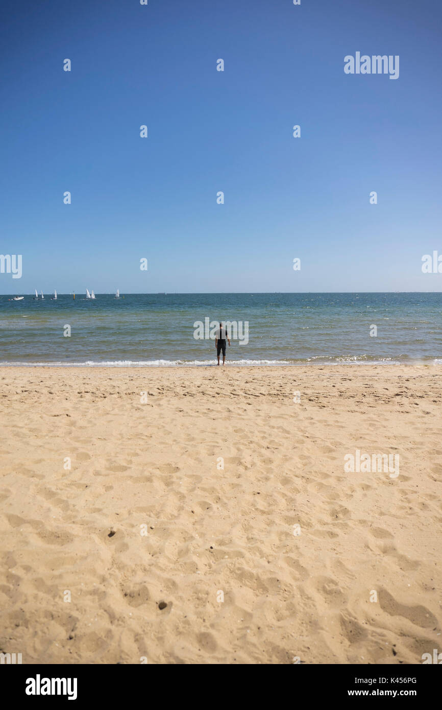 Mann in Schwarz auf dem Strand in der Nähe der Wasser aus der Ferne genommen Stockfoto