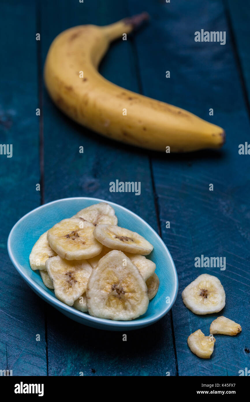 Getrocknete Bananen in einer Schüssel auf Benzin farbige Holz- Hintergrund. Stockfoto