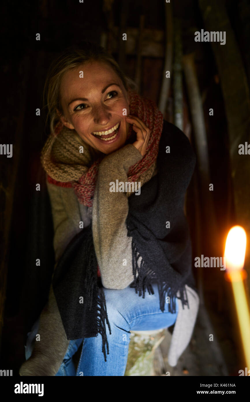 Blonde Frau sitzen auf einem Baumstamm, Lächeln, Kerze im Vordergrund. Stockfoto