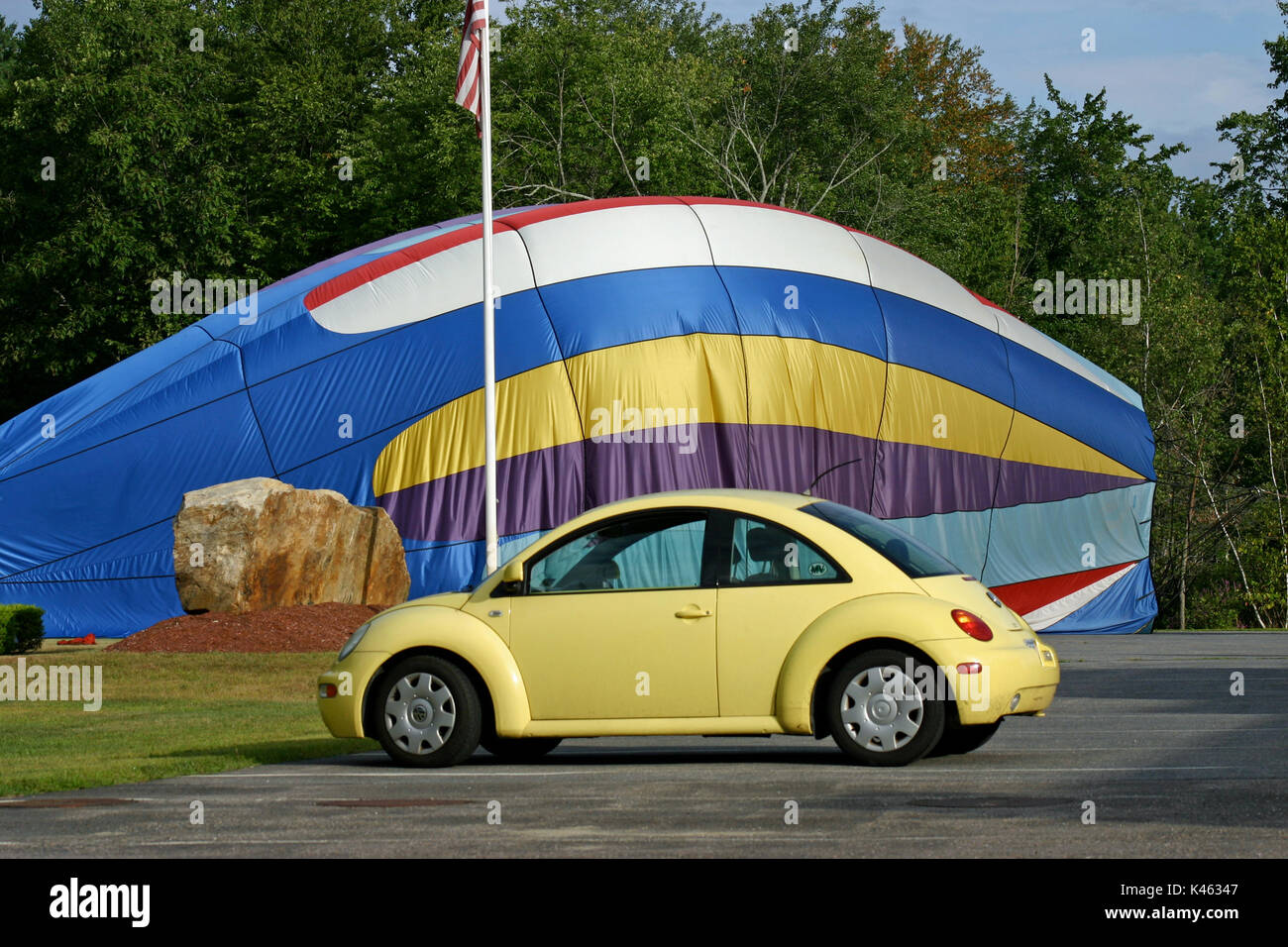 Ein gelber Volkswagen Beetle aus dem Jahr 1999 parkte vor einem teilweise aufgeblasenen, einstürzenden Heißluftballon Stockfoto