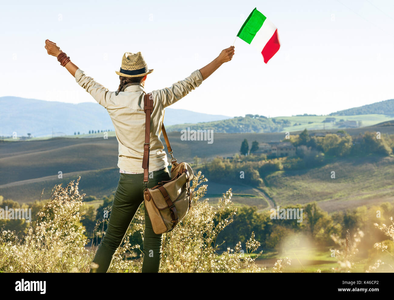 Entdecken Sie magische Ausblicke auf die Toskana. Hinter der jungen Frau Wanderer mit Tasche auf der Toskana Wanderung gesehen mit italienischer Flagge Freude Stockfoto