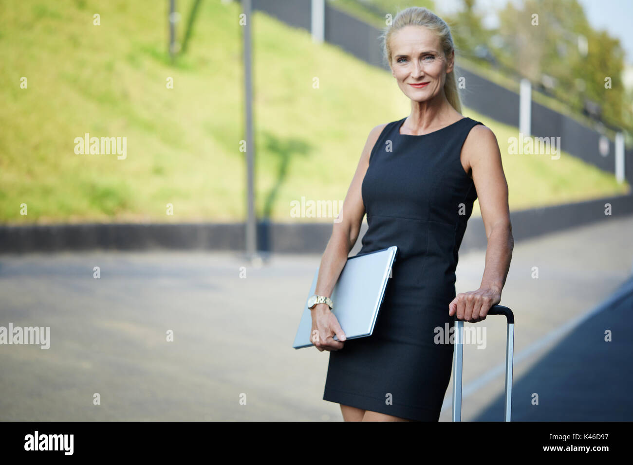 Gesicht portrait von zuversichtlich Geschäftsfrau holding Koffer Griff und Laptop. Stockfoto