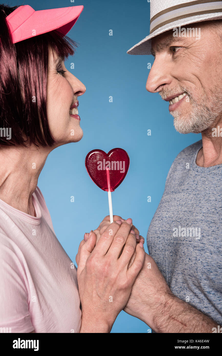 Stilvolle älteres Paar Hände mit Lollipop in Form von Herzen isoliert auf Blau Stockfoto