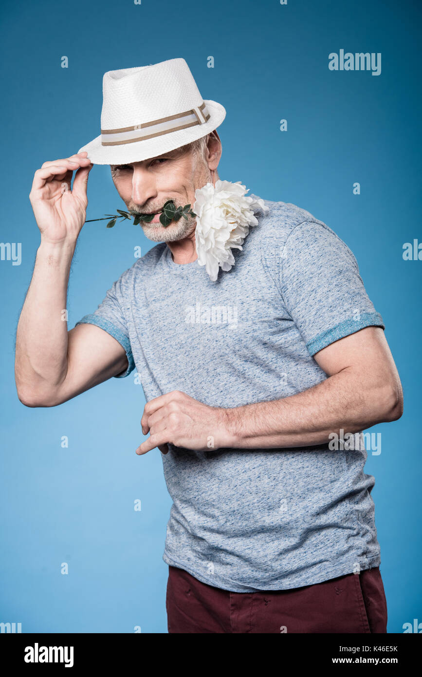Stilvolle gut aussehender älterer Mann mit Blume isoliert auf Blue posiert Stockfoto