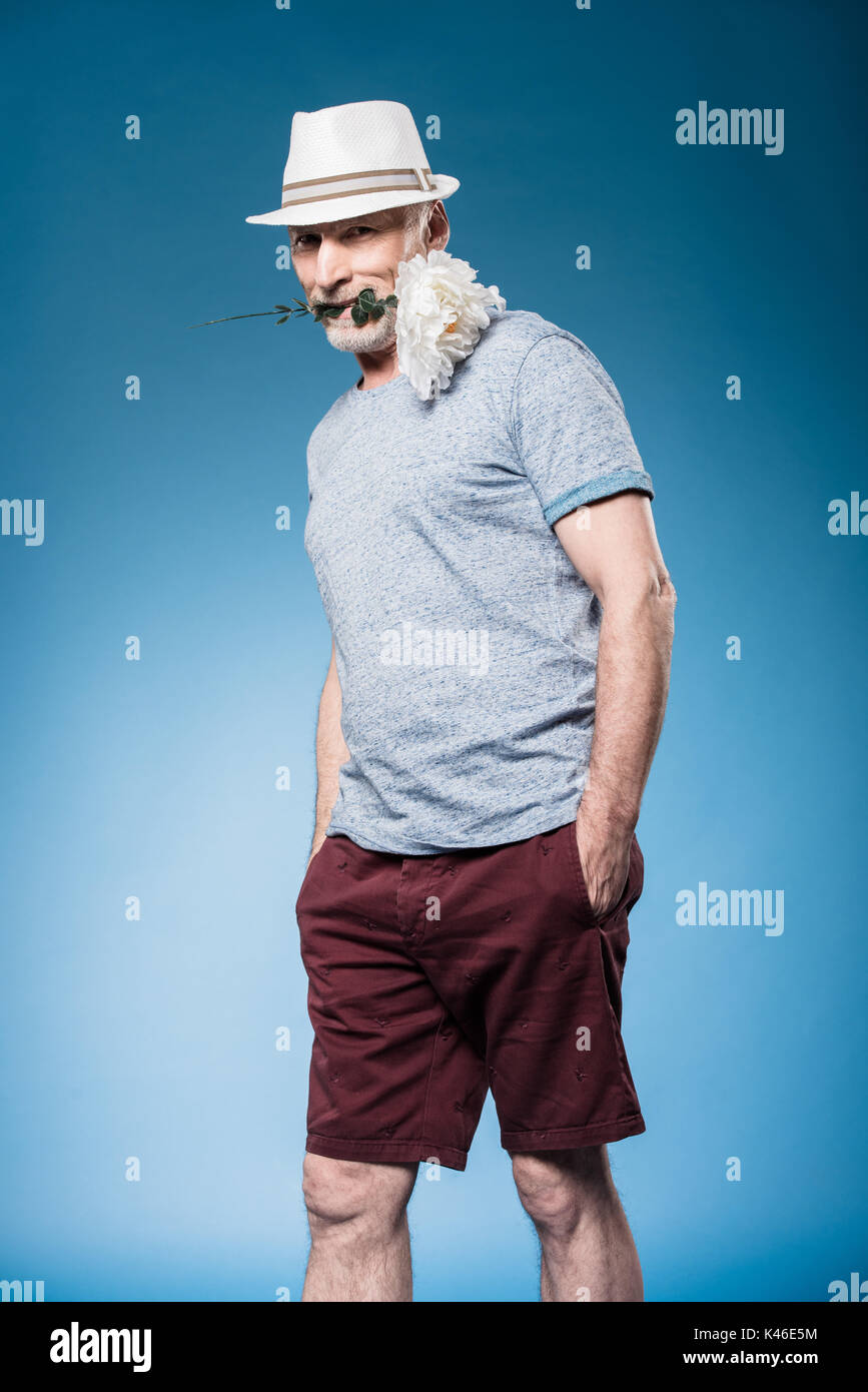 Modisch gut aussehender älterer Mann mit Blume im Mund isoliert auf Blue posiert Stockfoto