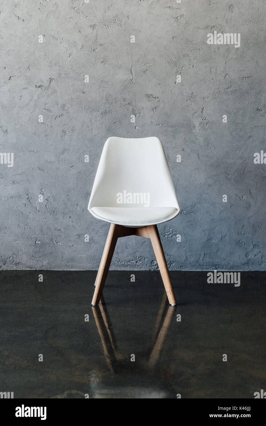 Leere moderner weißer Stuhl in der Nähe der graue Wand im minimalistischen Stil Stockfoto