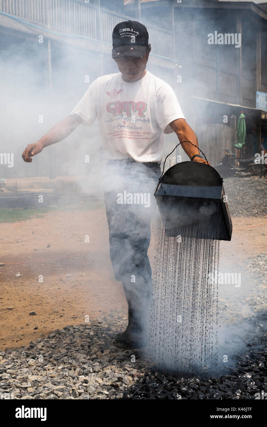 Bauarbeiter Instandsetzung Straße, gießt kochendes Bitumen von Hand auf aggregierten, Hsipaw, Myanmar Stockfoto