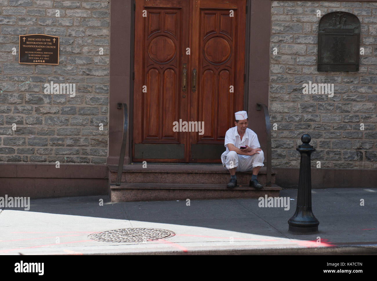 Ein Restaurant Arbeiter sitzt auf den Stufen der Kirche der Verklärung auf Mott Street in Chinatown in Manhattan. Die Kirche stammt aus dem Jahr 1801. Stockfoto