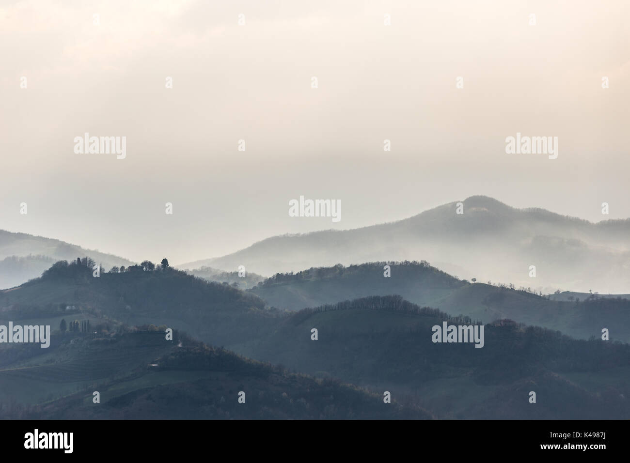 Grüne Hügel und Bäume im Vordergrund, Nebel und andere Hügel und Berge im Hintergrund Stockfoto