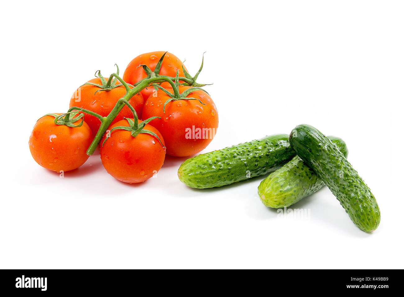 Nahaufnahme der Bündel der frischen roten Tomaten und mehrere grüne Gurke mit Wassertropfen von der Organic Farm auf weißem Hintergrund Stockfoto