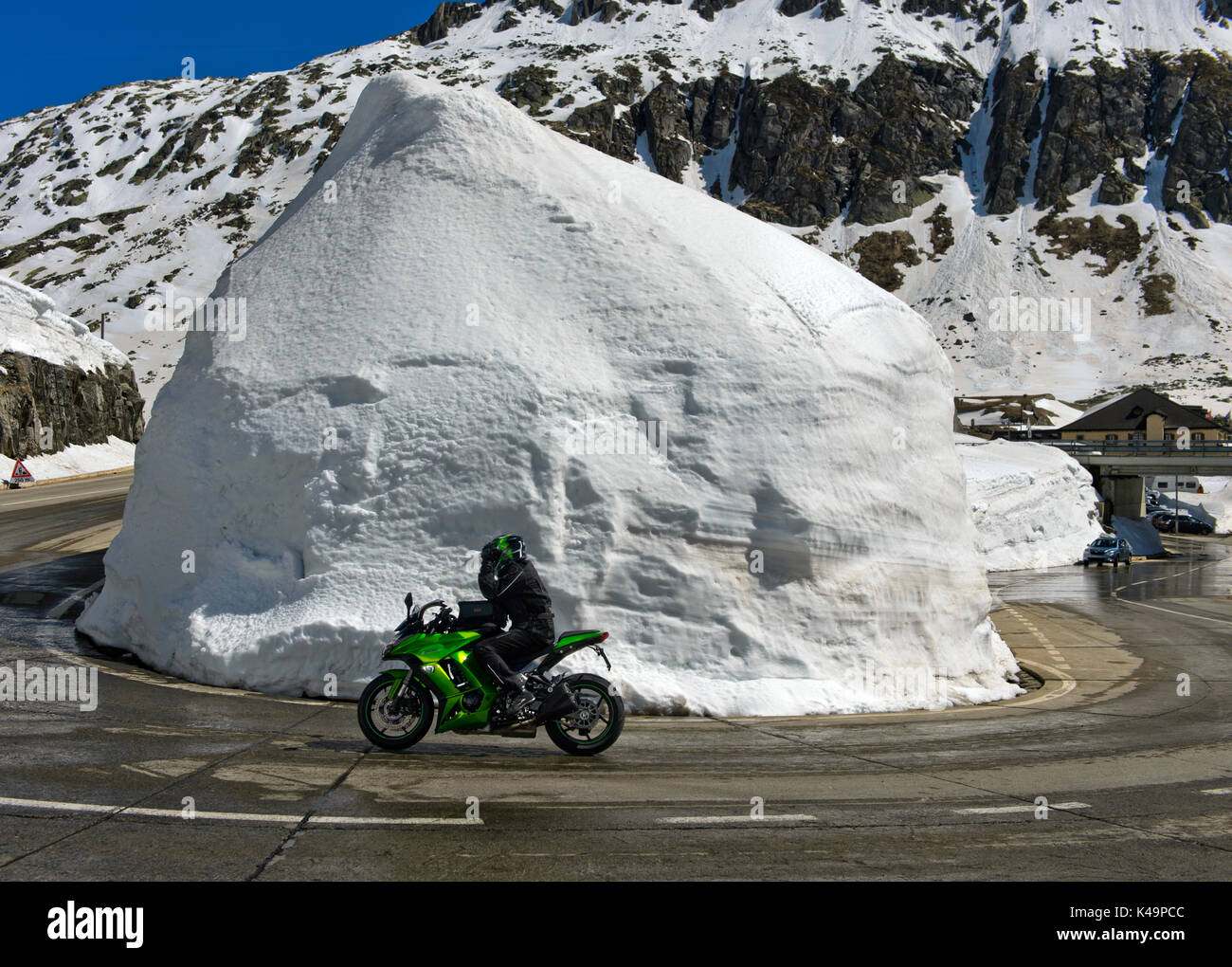 Motorbiker In einer scharfen Kurve um einen Haufen Schnee Auf dem Gotthard Pass Road, Airolo, Schweiz Stockfoto