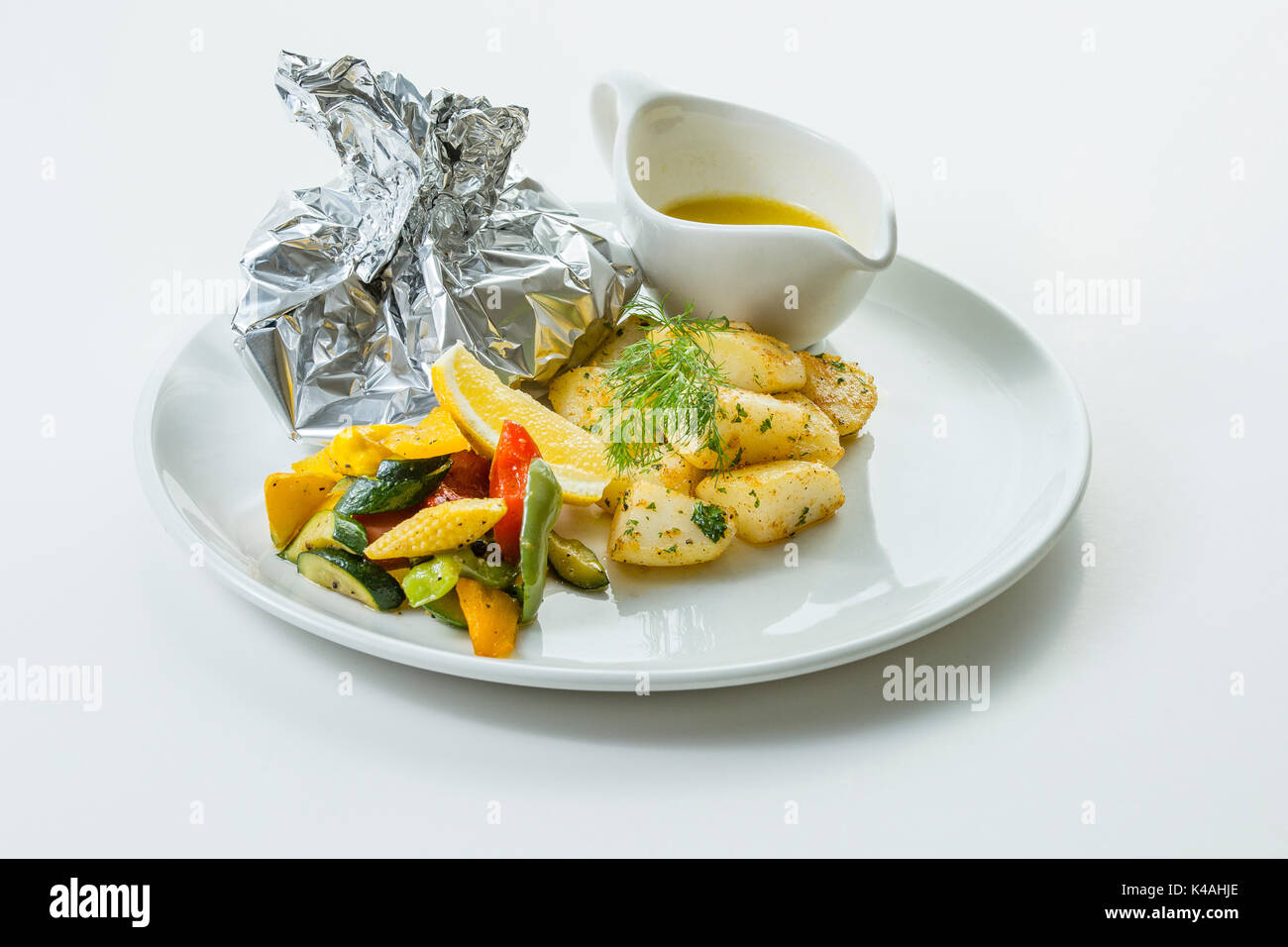 Gebackener Fisch in Alufolie mit Petersilienkartoffeln und Buttergemüse Stockfoto