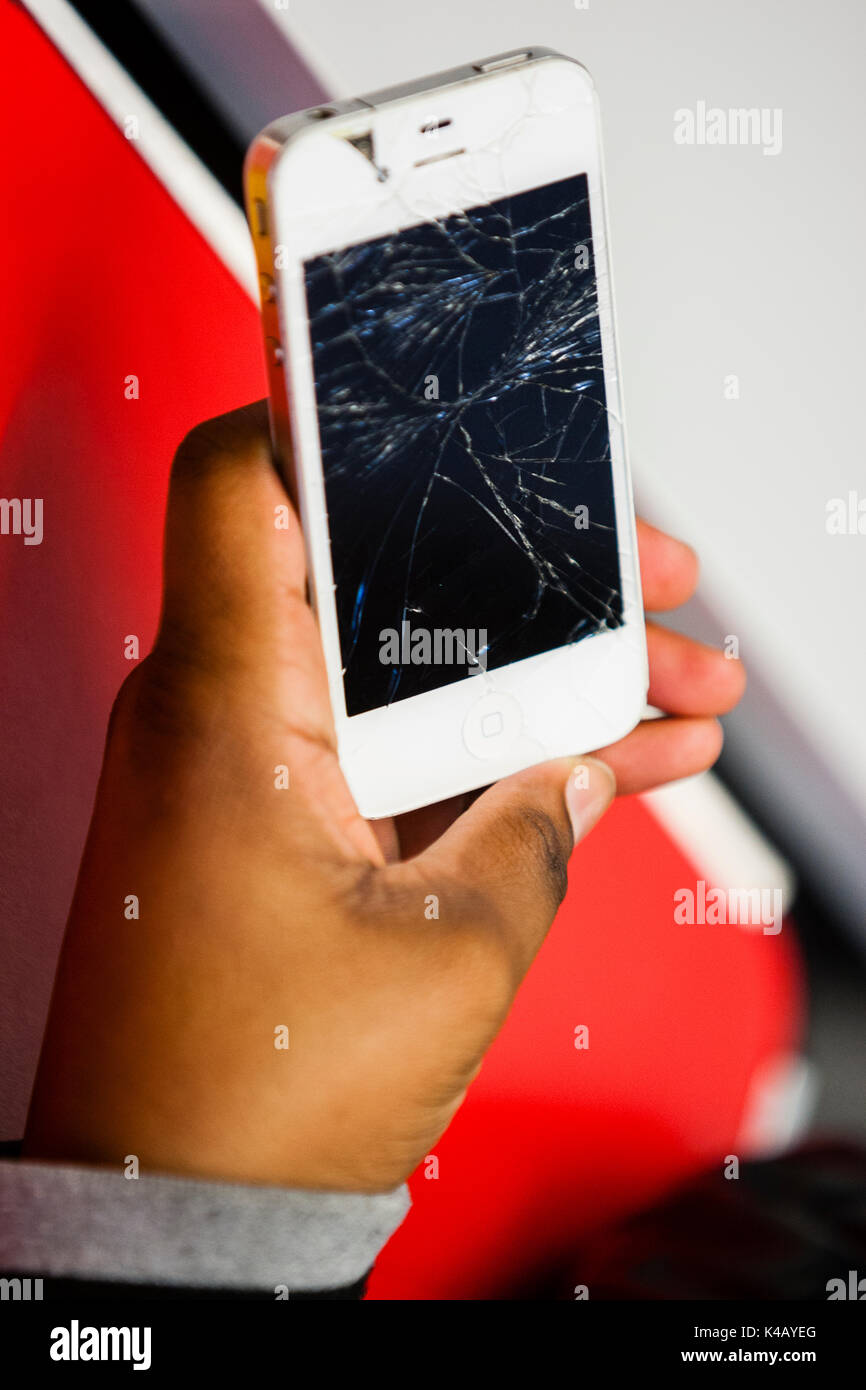 London, Großbritannien. Ein schwarzer Jugendlicher hält ein iPhone 4 mit einem zertrümmerten. Stockfoto