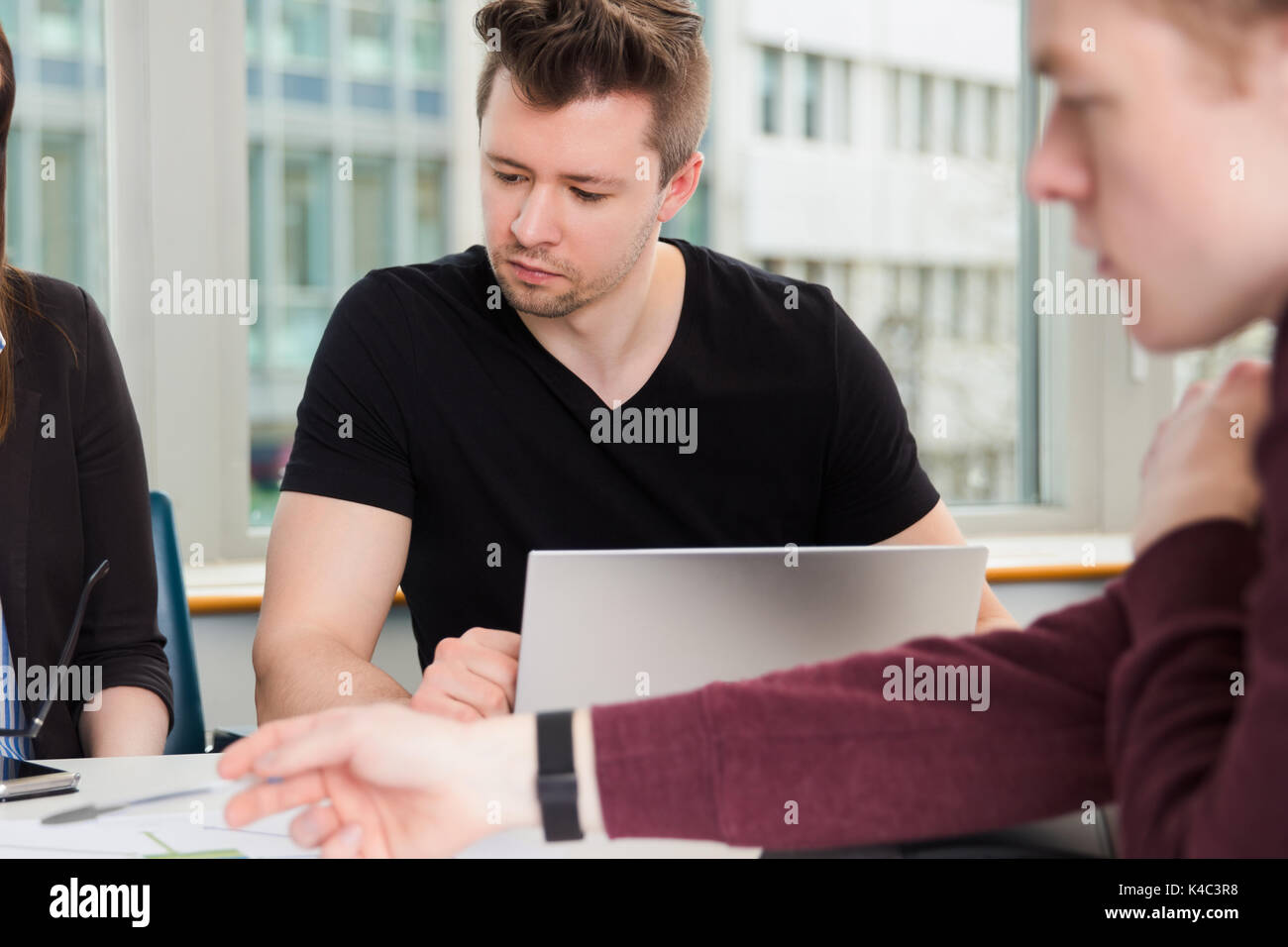 Geschäftsmann mit Laptop und Kollegen sitzen am Schreibtisch Stockfoto