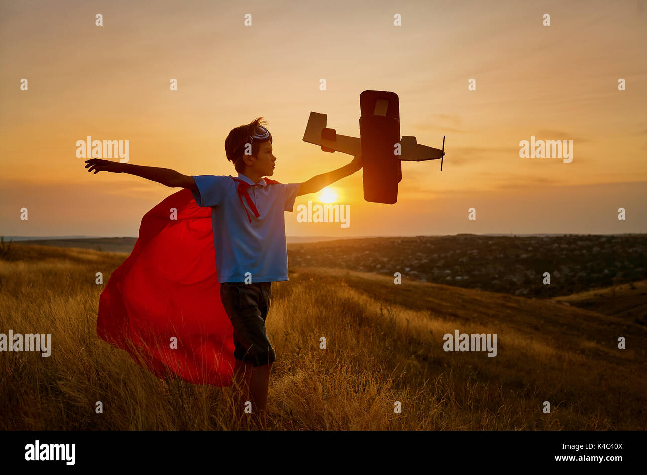 Eine glückliche junge in einen Superhelden Kostüm spielt mit einem Flugzeug. Stockfoto