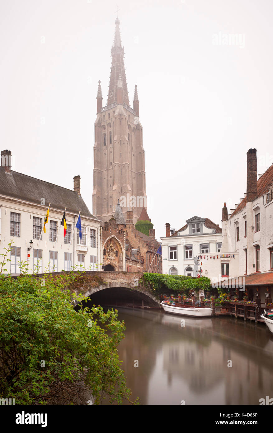 Blick auf den Turm der Liebfrauenkirche in Brügge, ein typisch nebligen Tag mit Reflexion in einem Kanal. Tagsüber lange Belichtung geschossen. Stockfoto