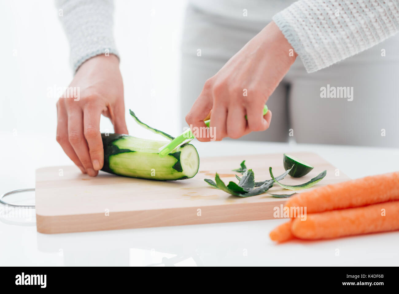 Frau Kochen gesund essen in Ihre Küche, sie ist Peeling ein frische Gurke auf dem Schneidebrett Stockfoto