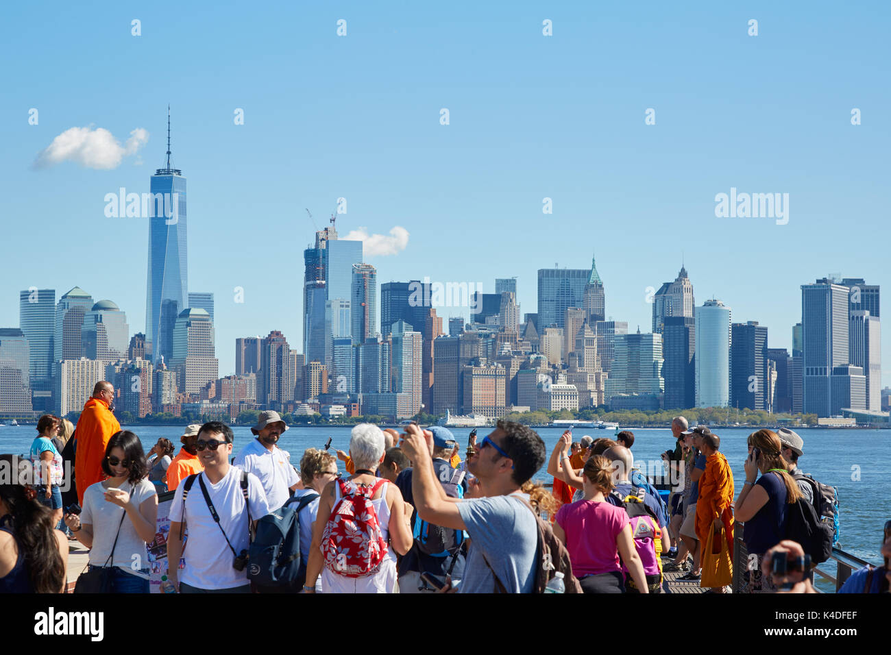 Menschen und Touristen fotografieren und mit Blick auf die Skyline von New York von Liberty Island an einem sonnigen Tag Stockfoto