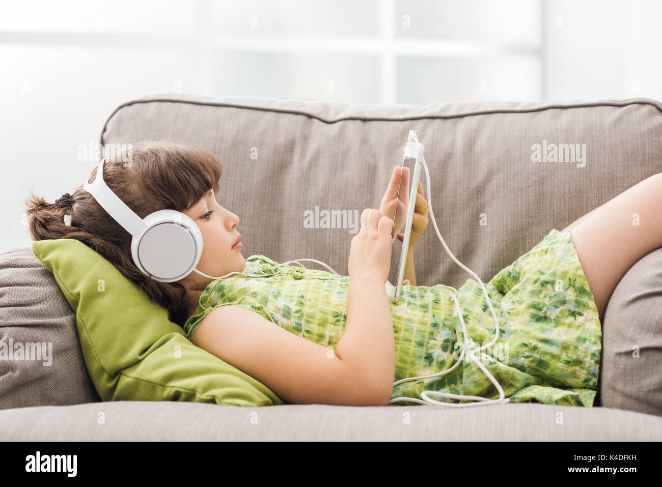 Süße Mädchen auf dem Sofa entspannen und mit einem digitalen Tablet, sie trägt Kopfhörer und Apps Stockfoto