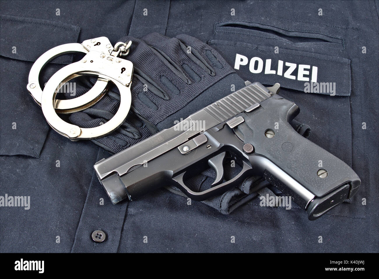 Pistole mit Handschellen und Handschuhe auf blauen Uniform Shirt mit 'Polizei' in deutscher Sprache auf es Stockfoto