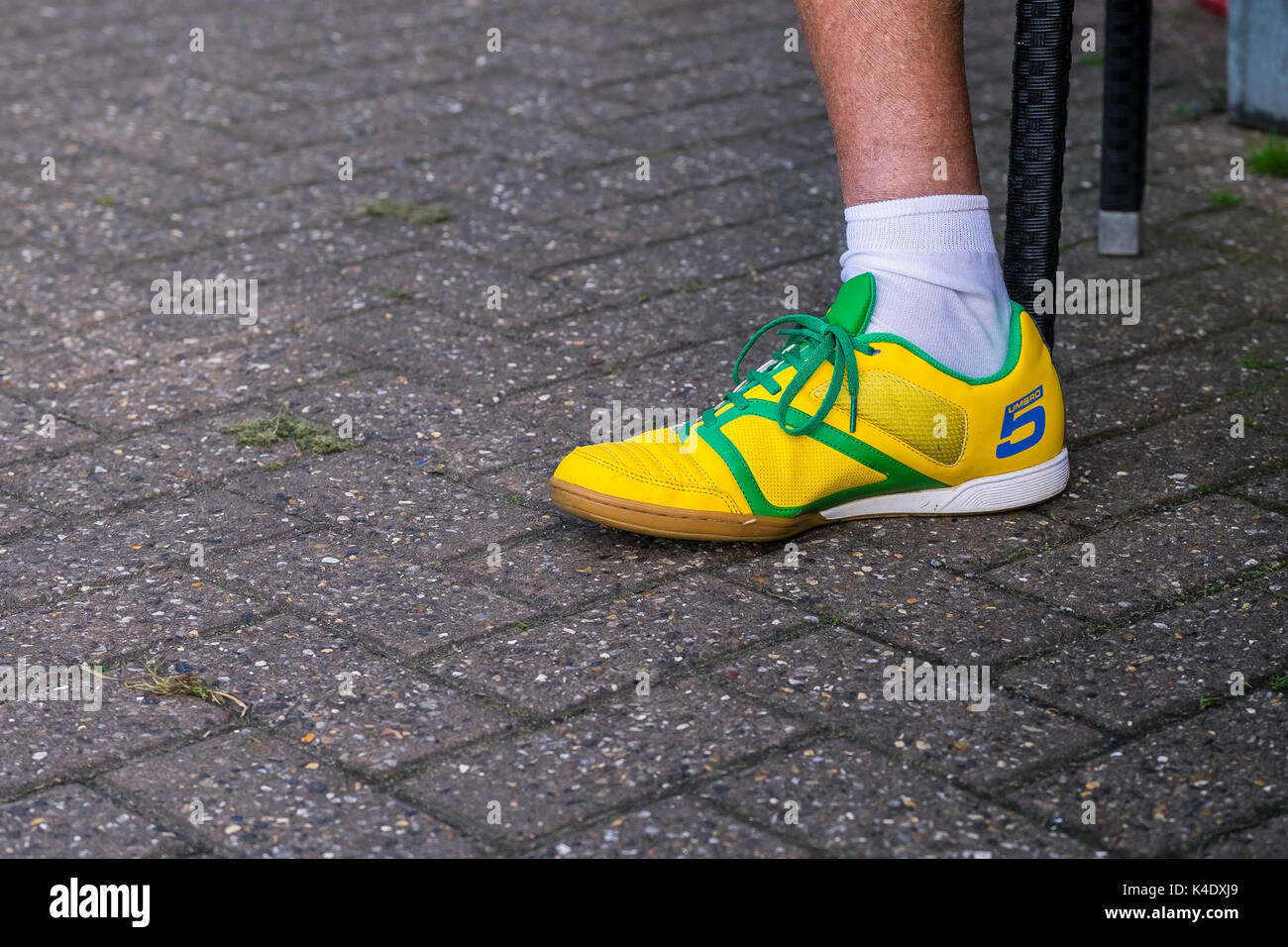 Ein linker Fuß trägt einen hellen gelben Umbro Trainer. Stockfoto