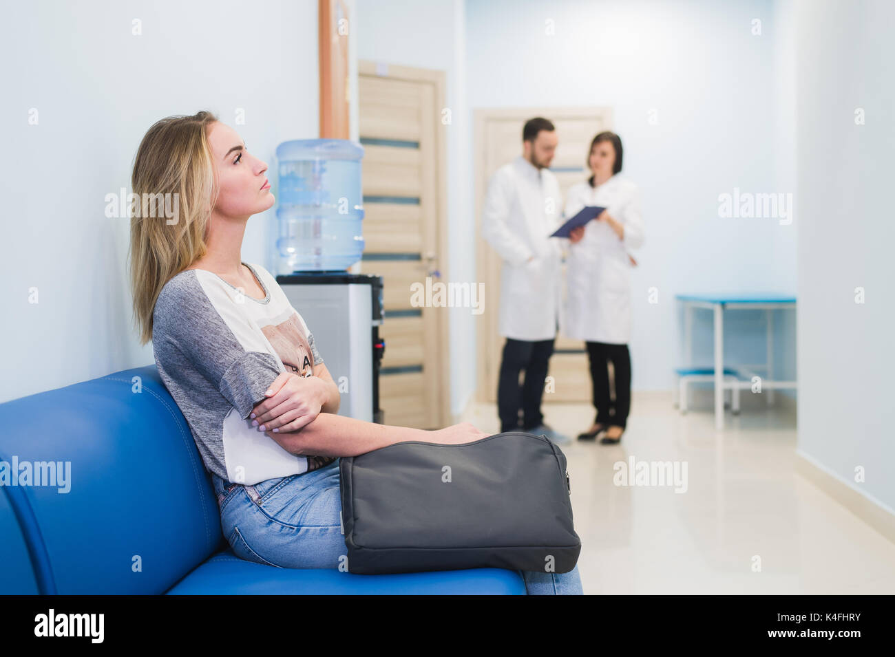 Junge Frau Füllung nervös sitzt am Krankenhaus Flur warten, während zwei Ärzte sprechen auf einem Hintergrund. Stockfoto