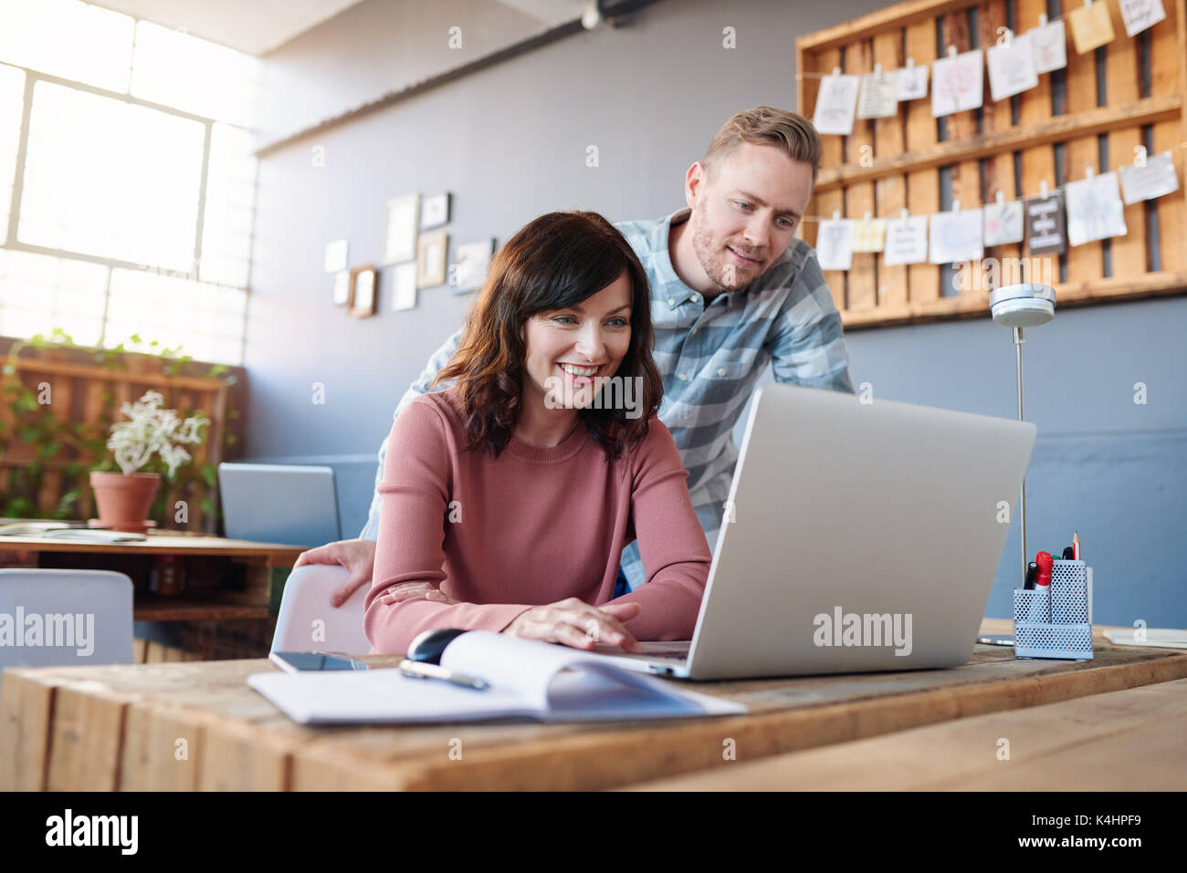 Zwei leger gekleidete junge Kollegen mit einem Laptop und miteinander sprechen, während Sie sich an einer Tabelle steht in einem modernen Büro Stockfoto