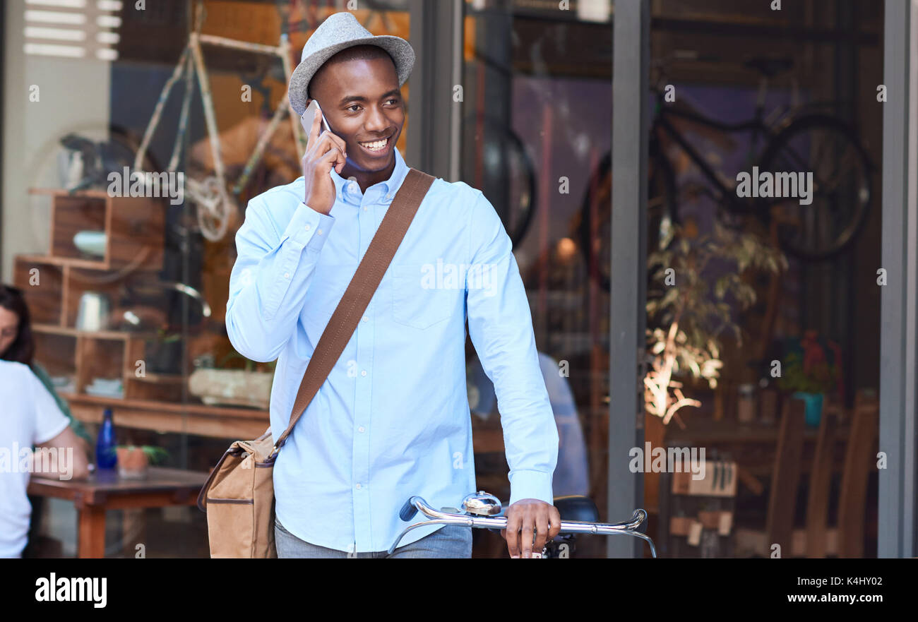 Stilvoll jungen afrikanischen Mann über sein Handy beim Gehen mit seinem Fahrrad eine Straße der Stadt angezogen Stockfoto