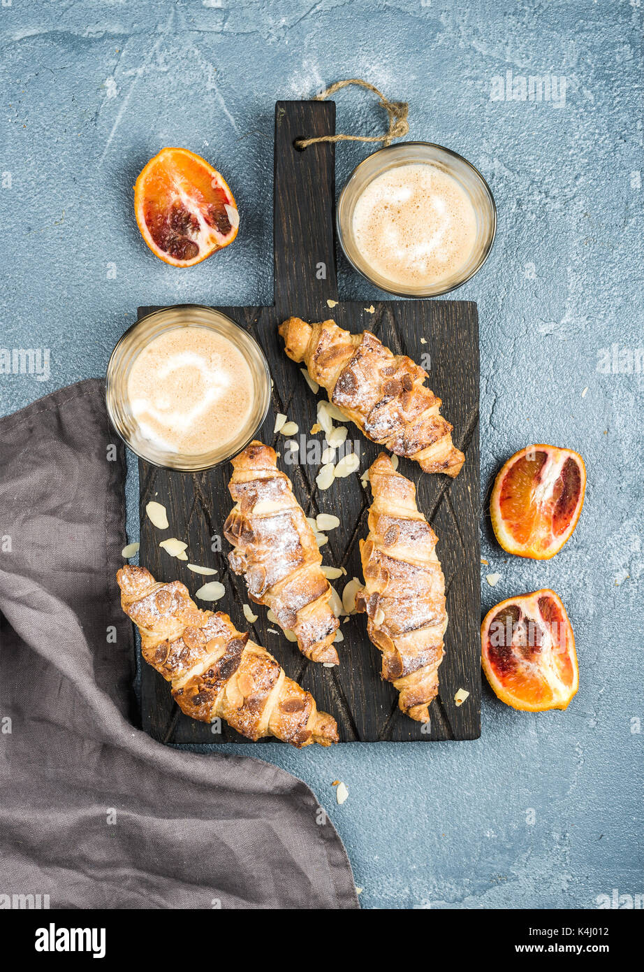 Traditionelle italienische Stil home Frühstück. Latte in Gläser, Almond Croissants und roten blutigen sizilianischen Orangen über konkrete strukturierte Tabelle Stockfoto