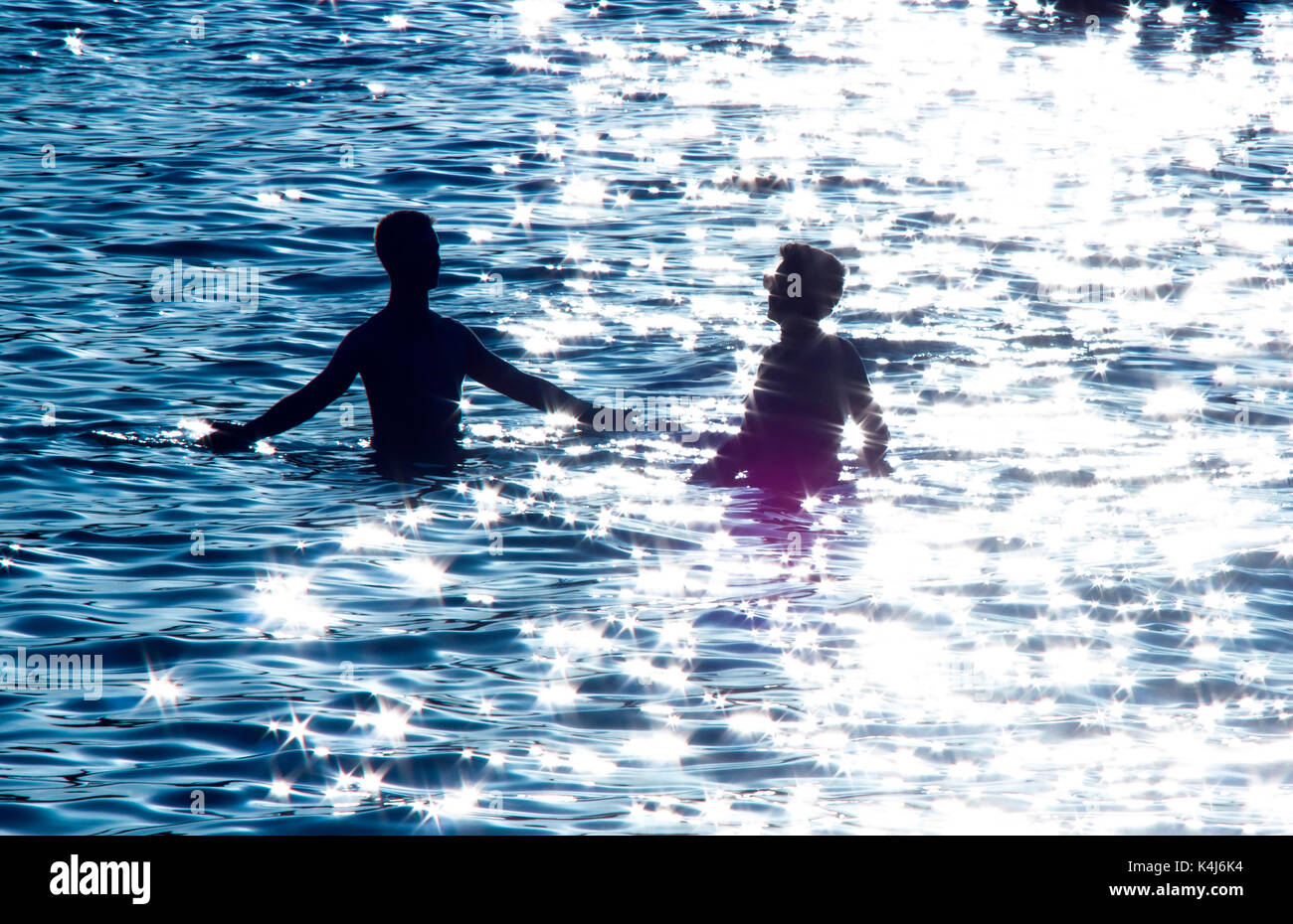 Silhouette von zwei jugendlichen Freunde in das blau glitzernde Meer teilen magische Momente und große Erwartungen an die unbeschwerte Jugend in moonlight Sommer Stockfoto