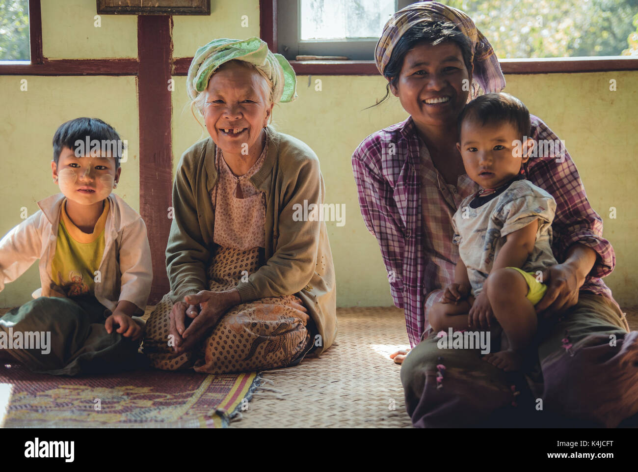 Die Menschen des ländlichen Lebens in der Landschaft von Myanmar. Großmutter, Mutter und ihre zwei Kinder auf dem Boden ihrer Heimat sitzen vor dem Essen. Stockfoto