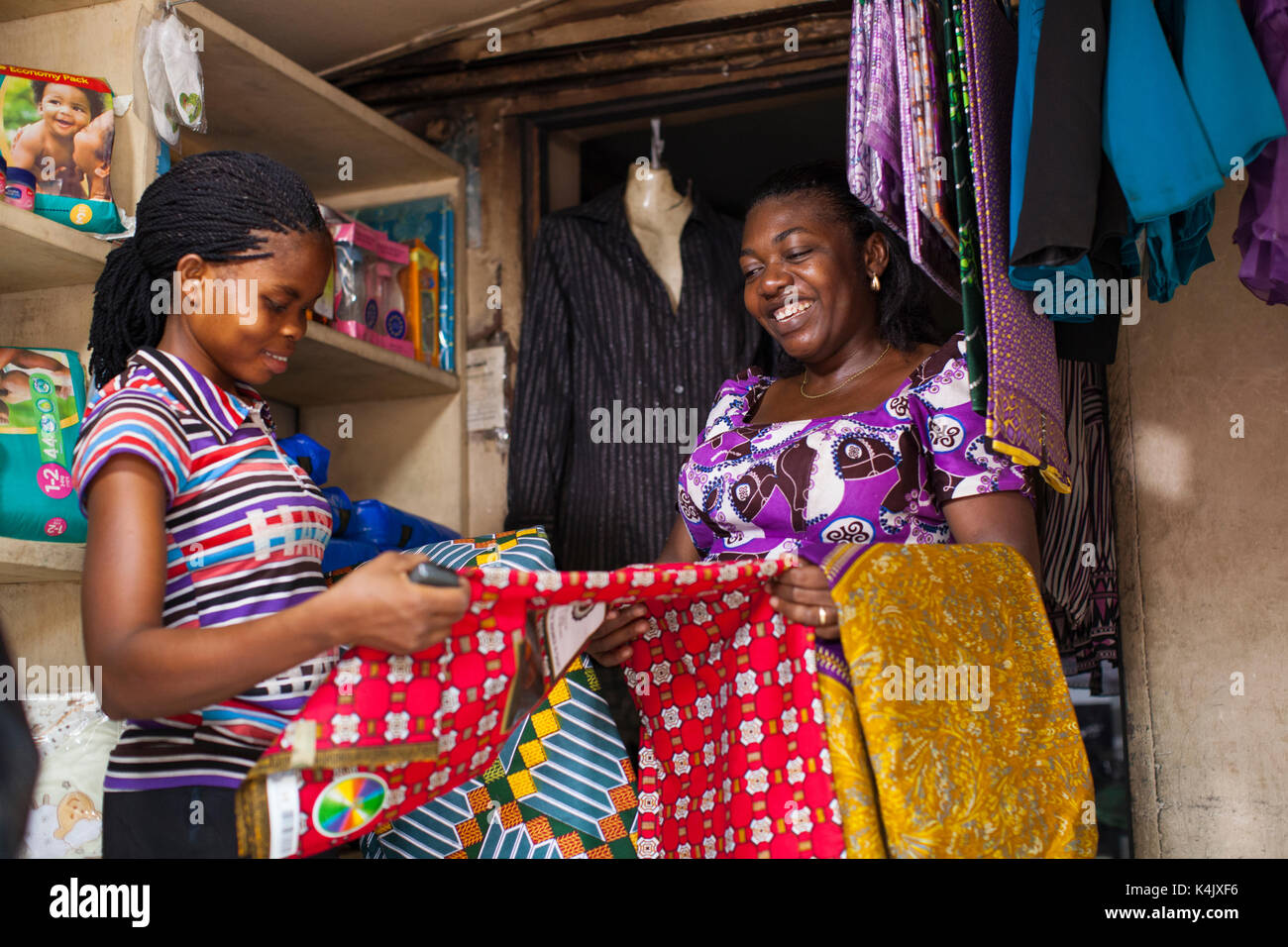 Eine weibliche Ladenbesitzer mit verschiedenen farbigen Materialien an einen potentiellen Kunden, Nigeria, Westafrika, Afrika Stockfoto