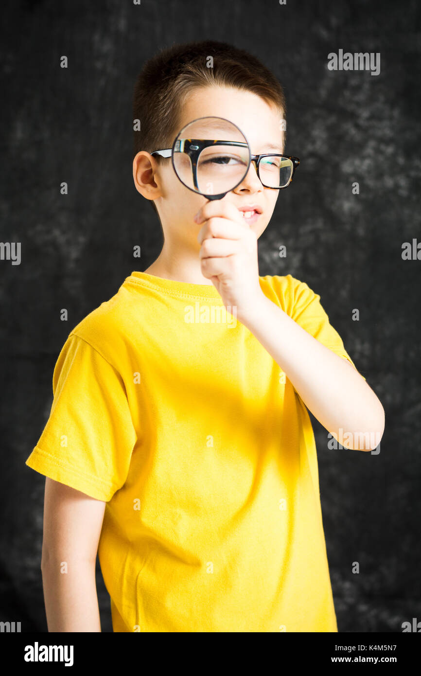 Junge Blick durch eine Brille und Lupe gegen den dunklen Hintergrund Stockfoto