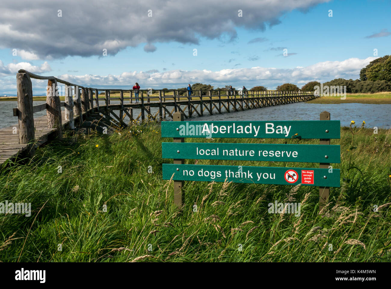 Menschen zu Fuß auf hölzernen Fußgängerbrücke über das Watt bei Flut, Aberlady Bay Nature Reserve, East Lothian, Schottland, Großbritannien, mit Schild, keine Hunde Stockfoto