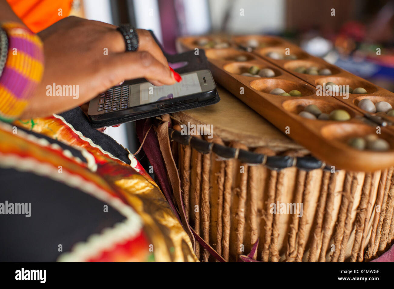 Eine Frau Typen eine Nachricht auf ihrem Mobiltelefon, während eine traditionelle nigerianische Spiel namens Ayo, Nigeria, Westafrika, Afrika Stockfoto