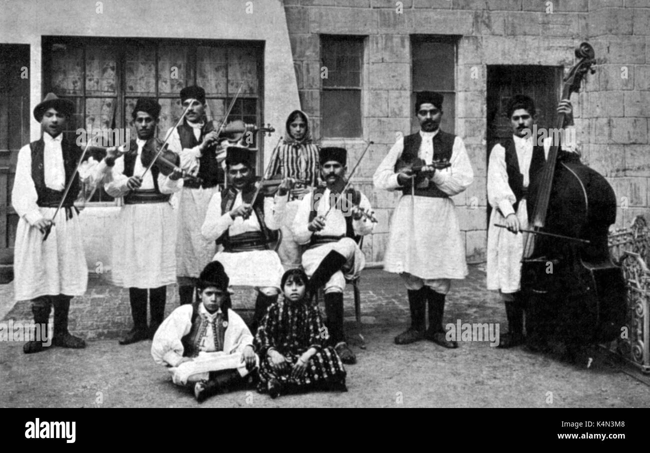 Serbische Musiker in der traditionellen Tracht spielen Violine und Kontrabass. Am Messegelände Earl's Court, Anfang des 20. Jahrhunderts. Traditionelle Kostüme. Stockfoto