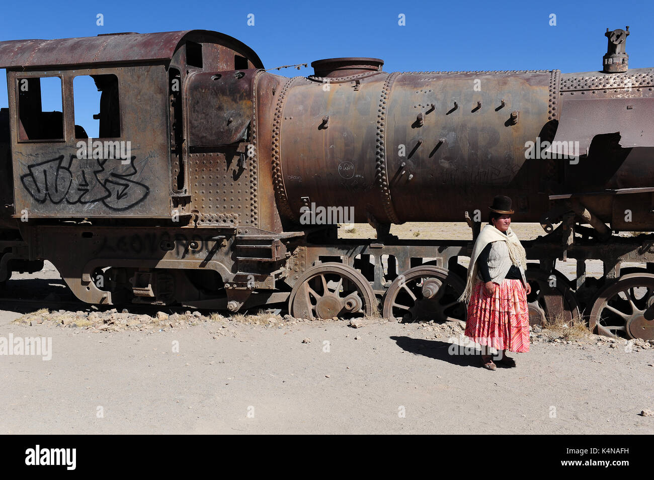 Einer bolivianischen Frau in traditioneller Kleidung vor einem vintage Lokomotive auf dem Friedhof vor den Toren der Stadt Uyuni, im südlichen Bolivien Stockfoto