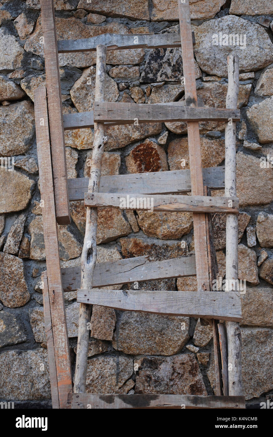 Rustikale Holzleitern gegen eine Mauer aus Stein Stockfoto