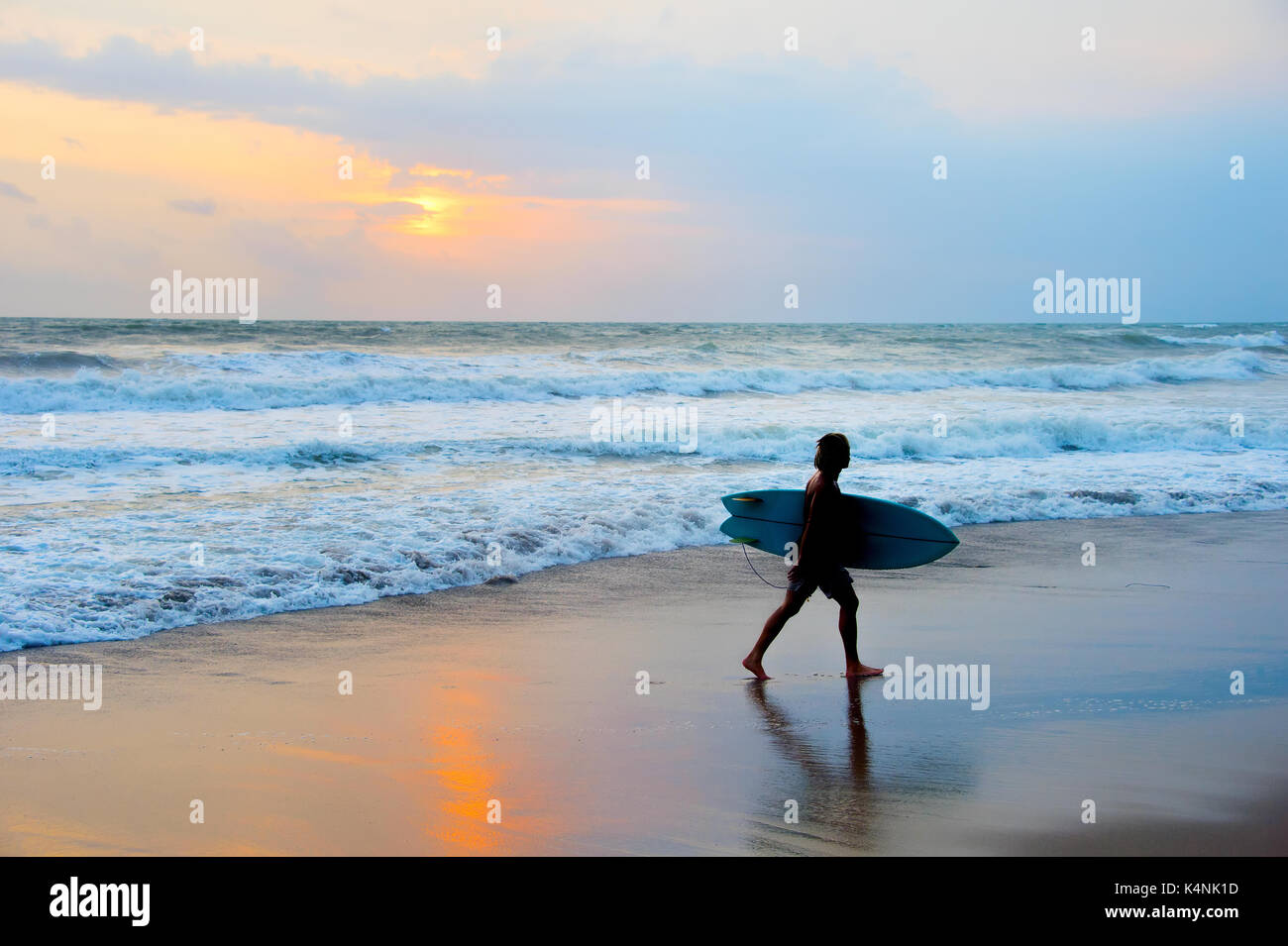 Dreadlocks Surfer am Strand mit Surfbrett bei Sonnenuntergang. Die Insel Bali Stockfoto
