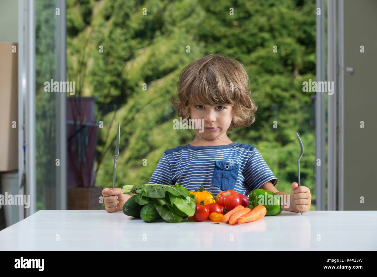 Cute little boy am Tisch sitzen und runzelte die Stirn über Gemüse essen, schlechte Essgewohnheiten, Ernährung und gesunde Ernährung Konzept Stockfoto