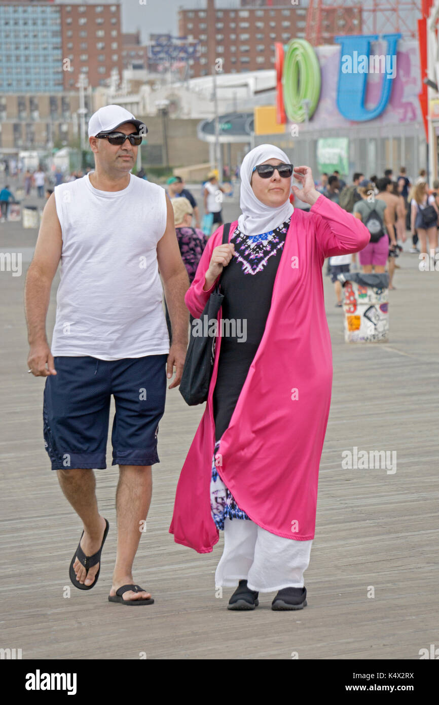 Ein muslimisches Paar auf der Promenade in Coney Island mit der Frau fast vollständig bedeckt, und der Mann in Shorts, Sandalen und ein Tank Top. Stockfoto