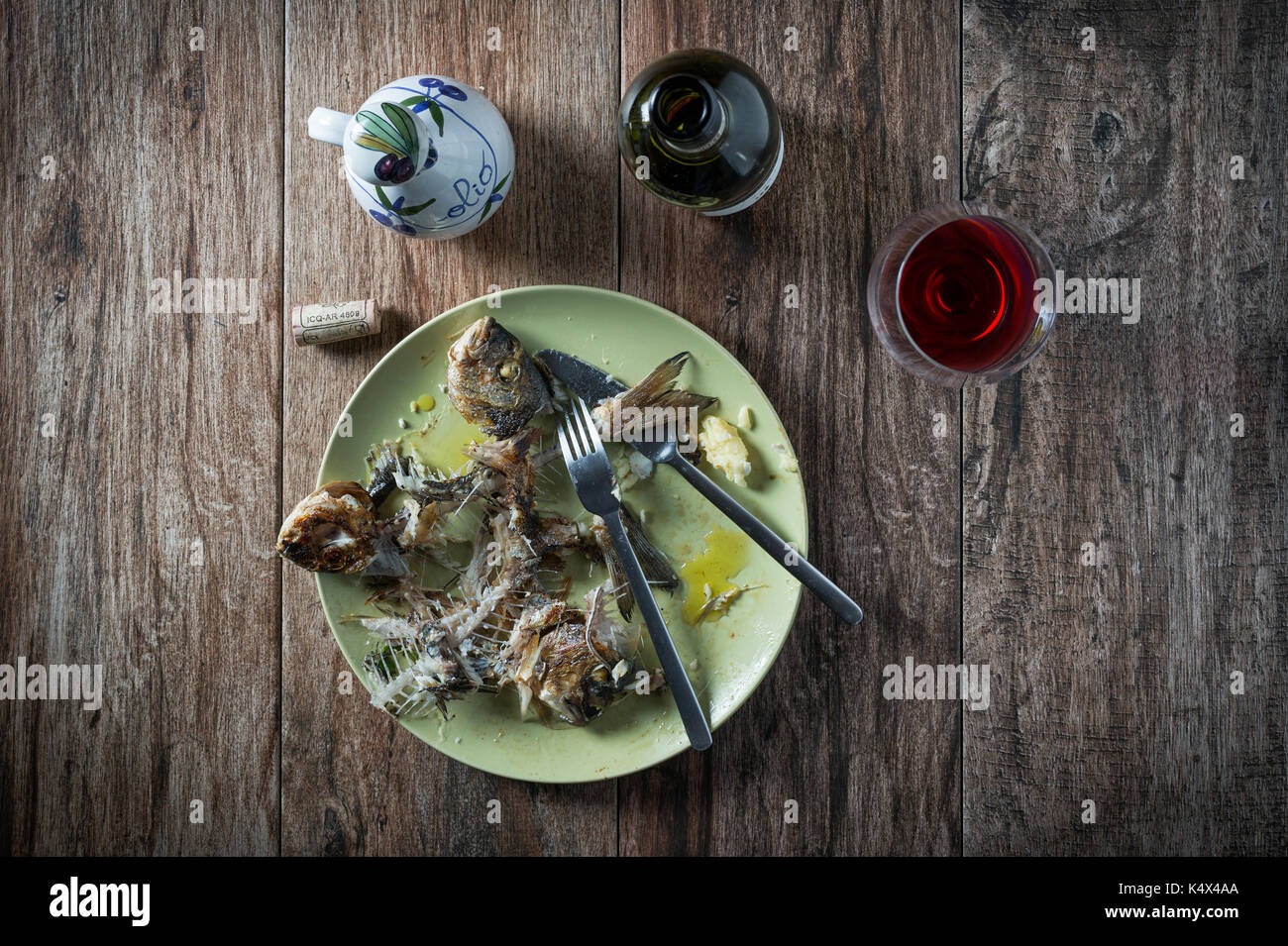 Fisch auf dem Teller mit Messer und Gabel, Glas und Flasche Wein. Beiseite stellen. Essensreste, Hausmüll entsorgt. Stockfoto