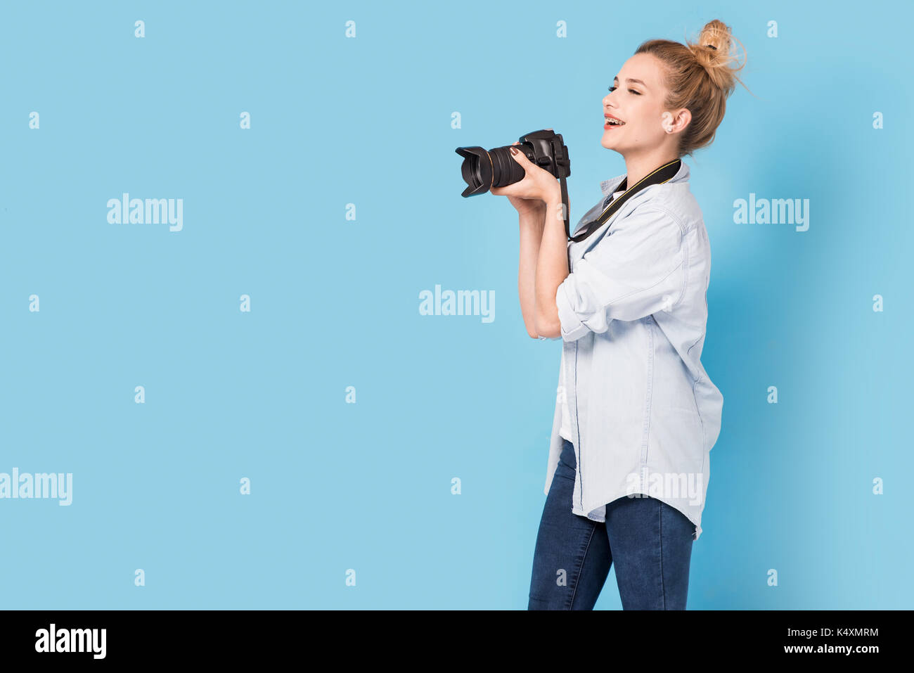Junge blonde Fotografin ist fotografieren. Modell isoliert auf einem blauen Hintergrund mit Textfreiraum Stockfoto