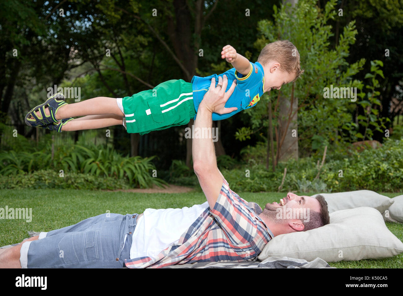 Vater spielt Flugzeug mit seinem Sohn im Garten Stockfoto
