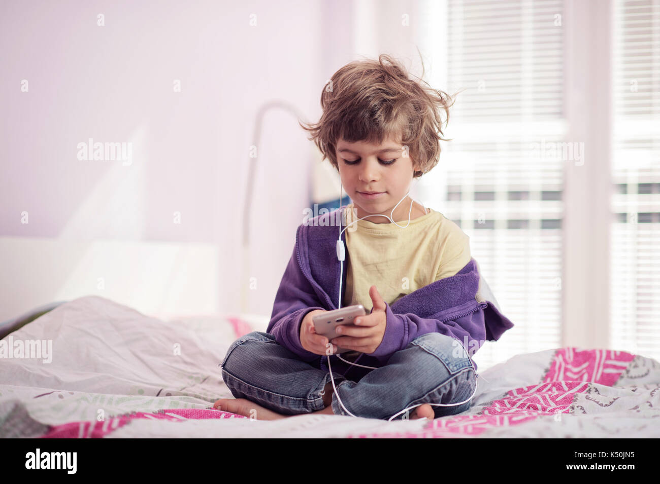 Kleiner Junge sitzt auf dem Bett Musik hören auf sein Smartphone. Stockfoto