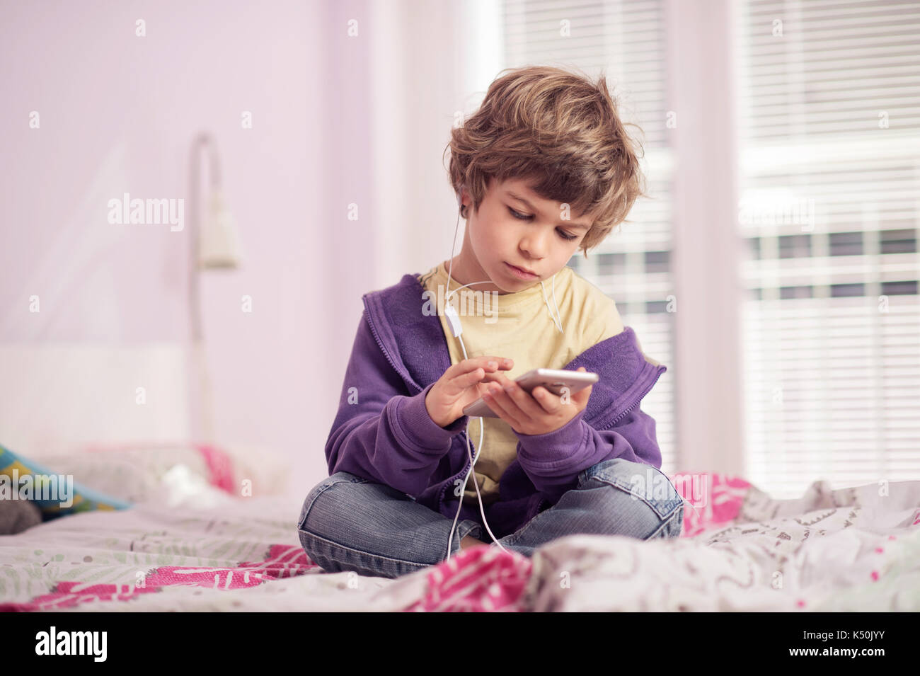 Kleiner Junge sitzt auf dem Bett Musik hören auf sein Smartphone. Stockfoto