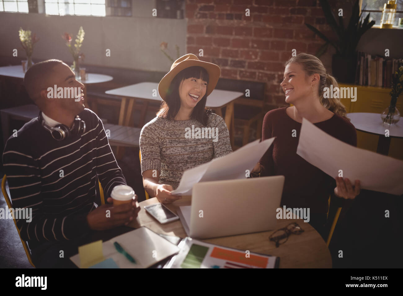 Fröhliche Creative Team sitzen mit Papieren und Laptop am Tisch im Café Stockfoto