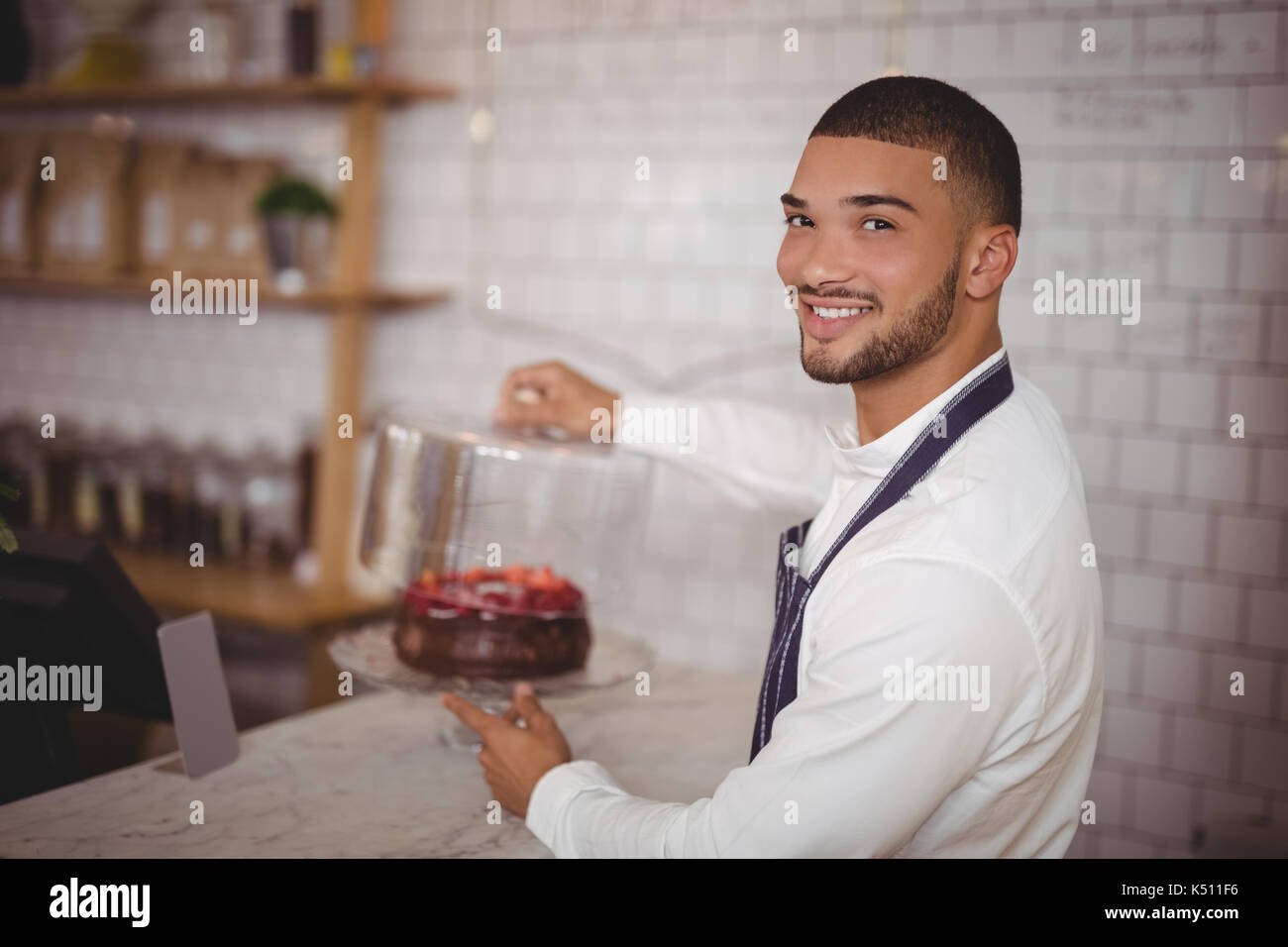 Seitenansicht Portrait von lächelnden jungen Kellner holding Kuchen am Zähler in Coffee Shop Stockfoto