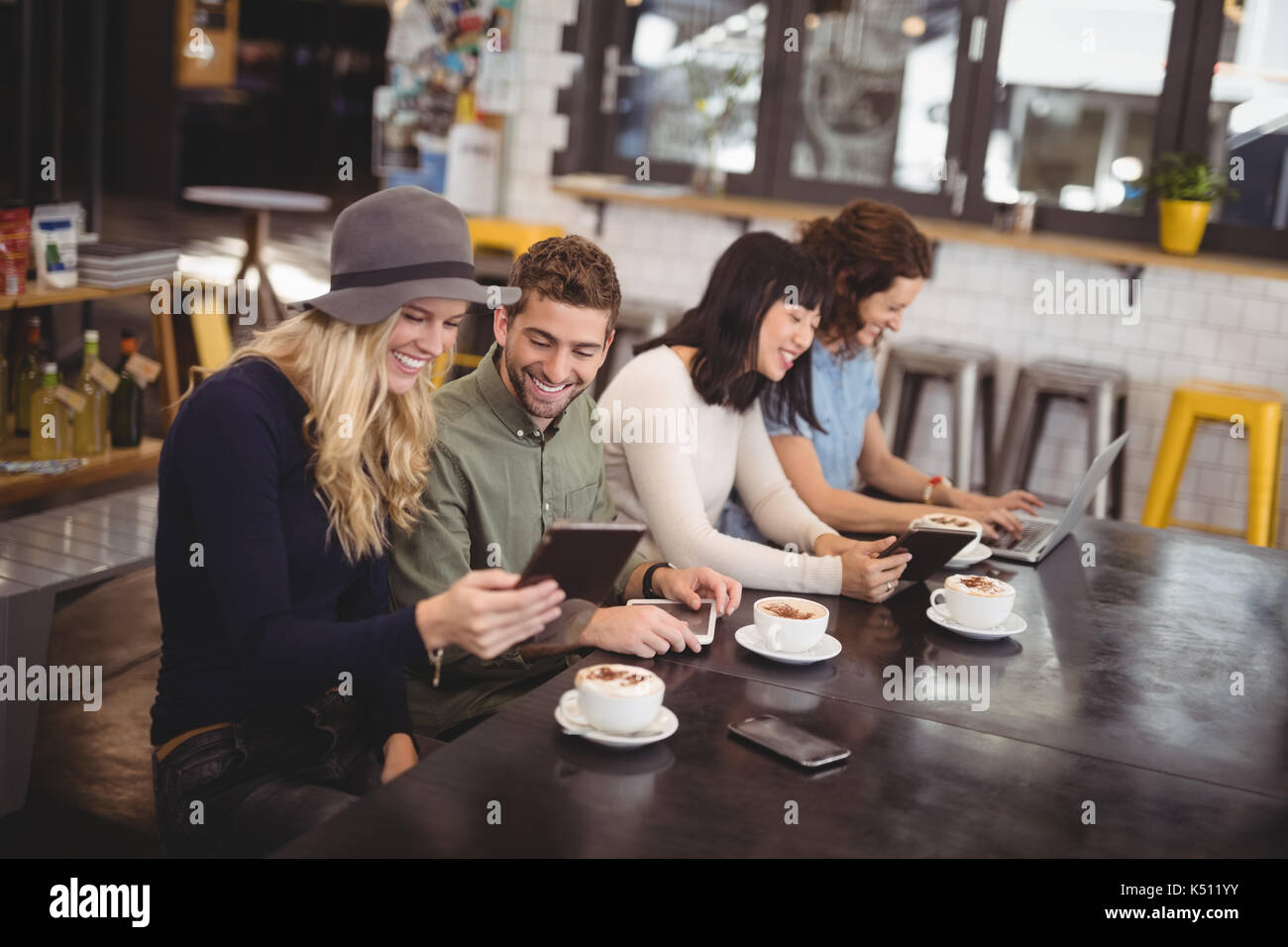 Hohe Betrachtungswinkel der glücklichen Freunde mithilfe von Technologien, beim Sitzen am Tisch im Café Stockfoto